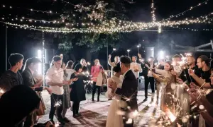 Para weselna tańczy wśród gości trzymających zimne ognie pod girlandami światełek.